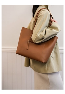 Detailed side view of a large brown leather tote bag with functional zipper pocket