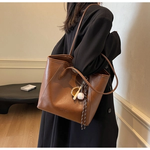 Detail of dark brown leather tote bag with baseball charm and textured finish on model