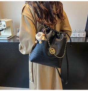 Close-up of black leather bucket bag with gold M logo, metal chain, and plush lamb charm