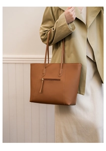 Detailed view of brown leather tote bag with zip pocket shown on a stylish model