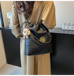 Detail of a black drawstring bucket bag with gold chain and plush sheep pendant charm