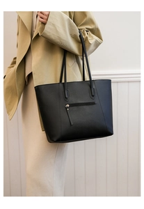 Macro detail of black leather tote bag showing exterior zipper pocket and matte texture