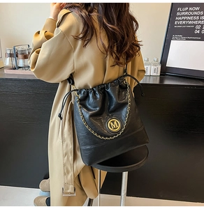 Detail view of black leather bucket bag with gold chain and M logo on trench coat