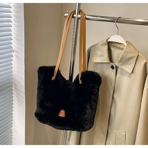 Detail of soft black faux fur tote bag with brown straps hanging on a metal hanger