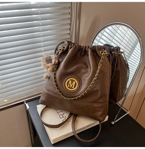 Detail of dark brown leather bucket bag with gold M logo, chain, and plush bear charm