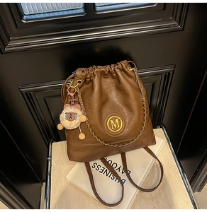 Detail of a brown leather drawstring bucket bag with gold M logo and bear charm