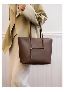 Close-up of a large dark brown leather tote bag with a back zipper pocket on a model