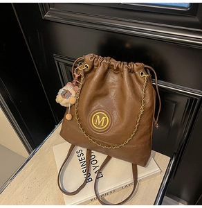 Detail of a brown drawstring bucket bag with golden M logo and a cute bear charm