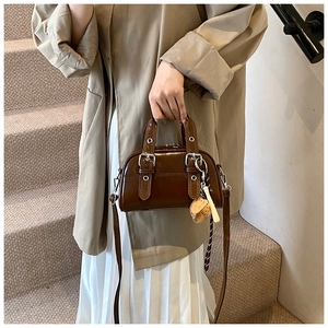 Détail du sac à main en cuir verni marron foncé avec boucles argentées et breloque fraise