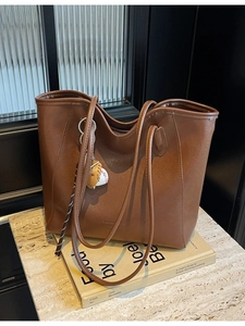 Large brown leather tote bag with baseball charm and slim shoulder straps on marble