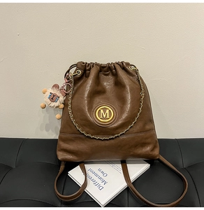 Close-up of brown leather bucket bag with gold M-logo and plush sheep pendant