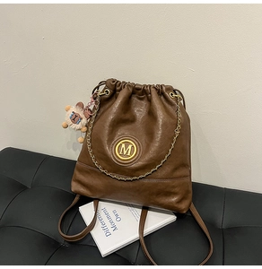 Detail of brown faux leather bucket backpack with gold M logo and cute alpaca charm