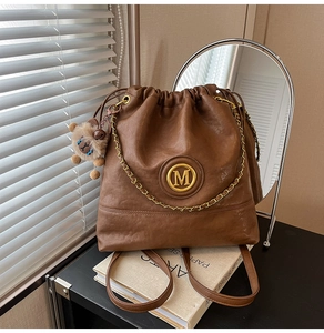 Brown bucket bag detail with gold metal M logo, chain accents and plush bear charm