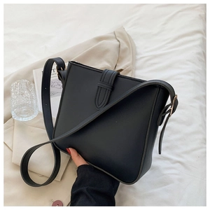 Minimalistische schwarze Leder-Eimertasche auf weißem Bett mit modernen Lifestyle-Requisiten