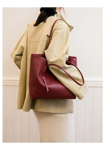 Burgundy tote bag worn with trench coat featuring side zipper pocket detail