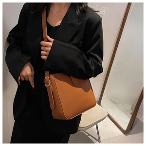 Braune Leder-Eimertasche mit goldener Hardware getragen über einem schwarzen Blazer