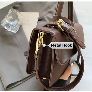 Detalle del bolso de cuero marrón con ganchos de metal dorado y correa de hombro ajustable