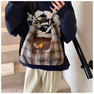 Détail du sac à carreaux avec rabat en cuir marron et boucle dorée avec la lettre N