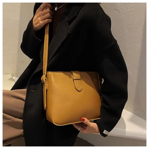 Detailansicht der senfgelben Leder-Eimertasche getragen mit einem schwarzen Wollmantel