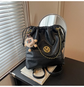 Detail of black PU leather bucket bag featuring gold M logo and plush animal charm