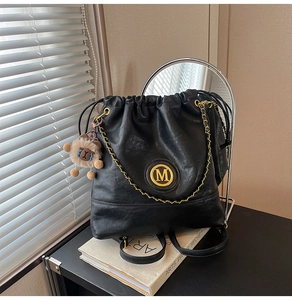 Detail of black leather bucket bag with gold M logo, chain, and lion charm pendant