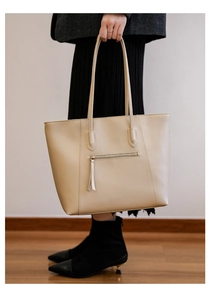 Detail of cream faux leather tote bag with metal zipper pocket and tassel on a model