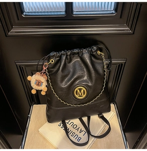 Close-up of black glossy bucket bag with golden M logo and plush lion pendant
