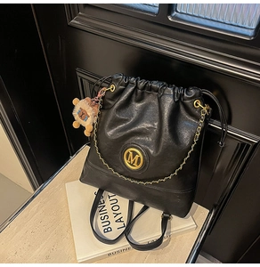 Close-up of black PU leather drawstring backpack with golden M logo and lion pendant charm