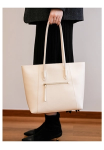Detail of a cream faux leather tote bag showing a sleek back zipper pocket and handle