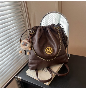 Detail of a brown leather drawstring bucket bag with gold M logo and sheep charm