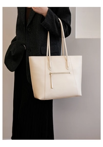Detail of beige tote bag with zipper pocket worn by model in a grey suit