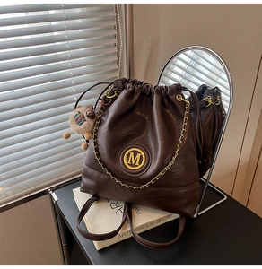 Detail view of brown leather bucket bag with gold M-logo and plush bear charm