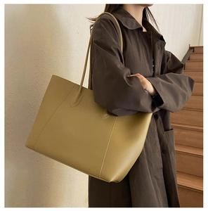 Minimalist light khaki leather tote bag carried by model wearing a dark brown trench coat