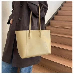 Detail of a large cream tote bag worn by a model on wooden stairs for daily commuting