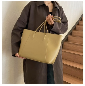 Model wearing a large khaki tote bag with long straps on wooden stairs for daily commute