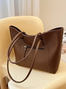 Bolso tote grande marrón con bolsillo de cremallera sobre una silla con luz suave