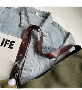 Close-up of dark green canvas bag with leather strap and silver metal grommet detail