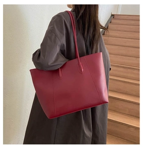 Minimalist deep red leather tote bag shown on shoulder over a brown coat by stairs