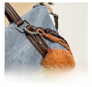 Detail show of blue denim bucket bag with brown leather handles and teddy bear charm