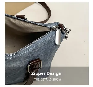 Detail of silver metal zipper and brown leather handle on blue denim bucket bag