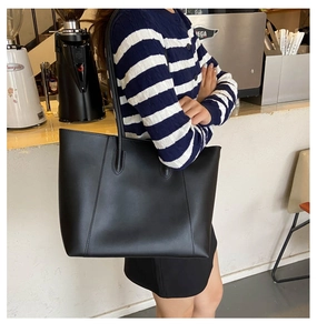 Close-up of a stylish black PU leather tote bag worn as an underarm bag in a cafe setting