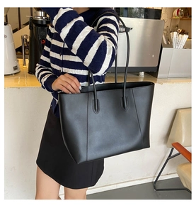 Close-up of minimalist black matte leather tote bag worn by model in a cafe setting