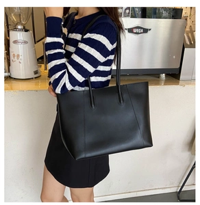 Minimalist black tote bag shown on shoulder in a stylish cafe setting for daily commute