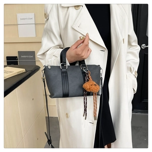 Detailed view of gray bucket bag with teddy bear charm and crossbody strap