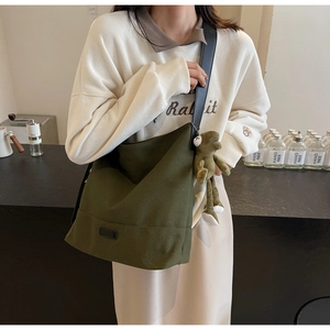 Olive green canvas crossbody bag with wide shoulder strap and plush frog pendant charm