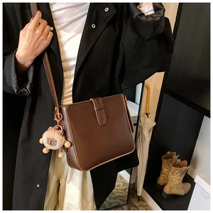 Détail du sac à bandoulière marron foncé avec charm en peluche et fermoir à boucle