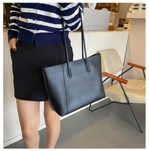 Close-up of a large black minimalist tote bag carried over the shoulder by a model