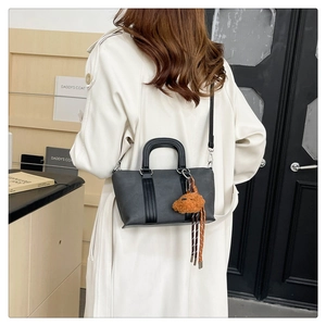 Detail of a black matte bucket bag with a brown teddy bear charm worn with an ivory coat