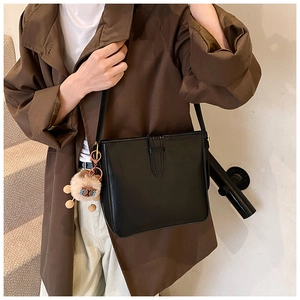 Détail d'un sac seau en cuir noir brillant avec un petit ours en peluche brun