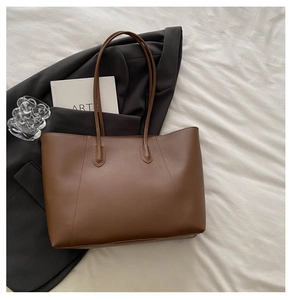 Detail shot of vintage brown leather tote bag with fine stitching on white bedding